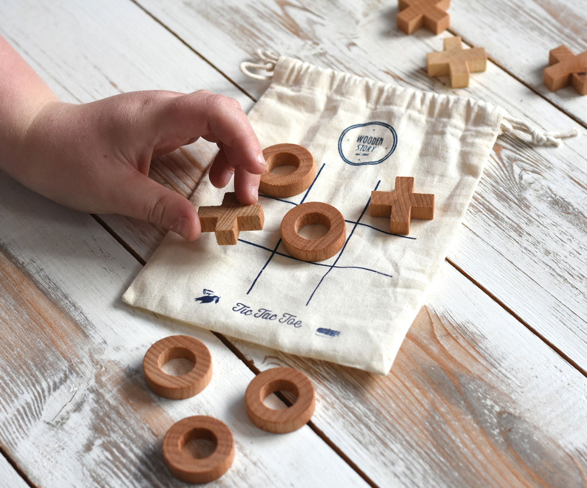A close up of a child's hand playing with the Wooden Story Tic Tac Toe game.