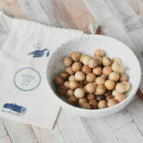 The small wooden balls that come  with the Wooden Story Montessori Number Tracing Board placed in a small white ceramic bowl. A small cotton drawstring storage bag can be seen by the side of the bowl.