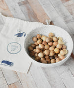 The small wooden balls that come  with the Wooden Story Montessori Number Tracing Board placed in a small white ceramic bowl. A small cotton drawstring storage bag can be seen by the side of the bowl.
