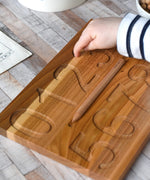 A close up of a child's hand using their finger to trace the number 3 on the Wooden Story Montessori Number Tracing Board.