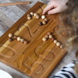 The Wooden Story Montessori Number Tracing Board being used with the supplied small wooden balls. A child can be seen placing the balls on the number indents on the board.