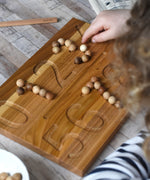 The Wooden Story Montessori Number Tracing Board being used with the supplied small wooden balls. A child can be seen placing the balls on the number indents on the board.