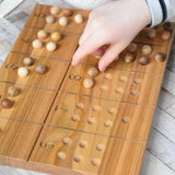 A close up of a child's hand placing wooden balls on the Wooden Story Montessori Number Tracing and Counting Board. The counting side of the board features the numbers from 1 to 10 alongside a corresponding number of indents that the small wooden balls can sit on.