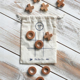 The Wooden Story Tic Tac Toe game with the bag and pieces placed on a wooden surface.