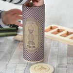The decorated tube gift box that contains the decorated Wooden Story Stacking Toy Stick Purple Number 6 Figure. The rigid tube has a wooden disc lid.