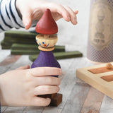 A close up of a child's hand playing with the Wooden Story Stacking Toy Stick Purple Number 6 Figure. They are lifting the maroon red coloured hat shaped piece off the top.