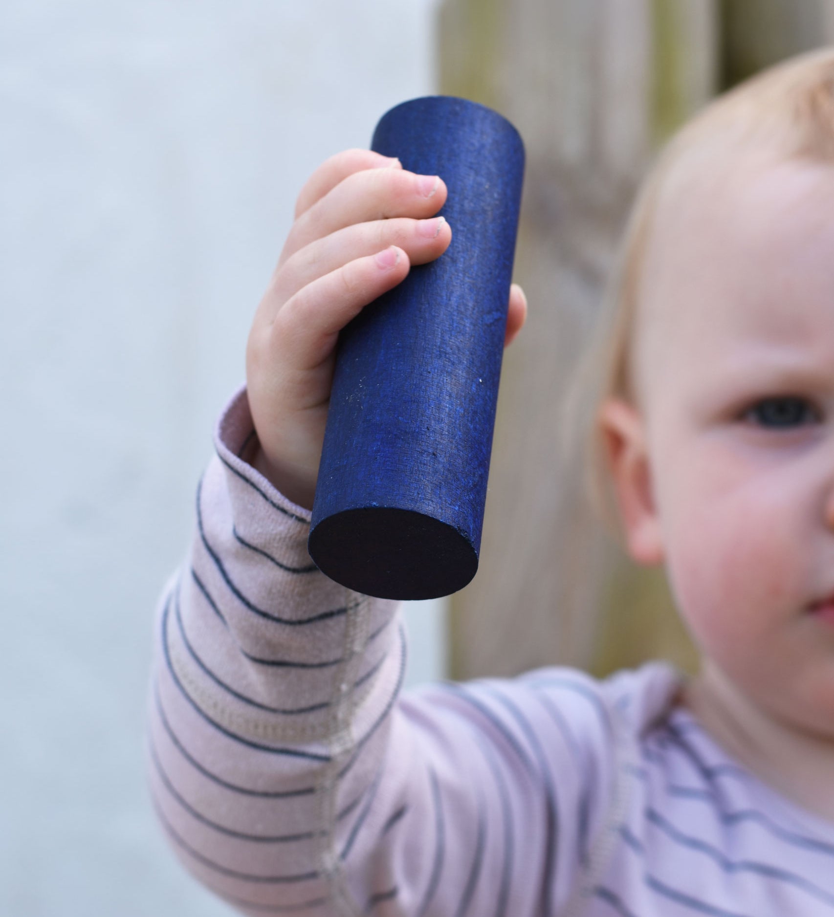 A close up of the large blue cylinder block in a young child's hand. 