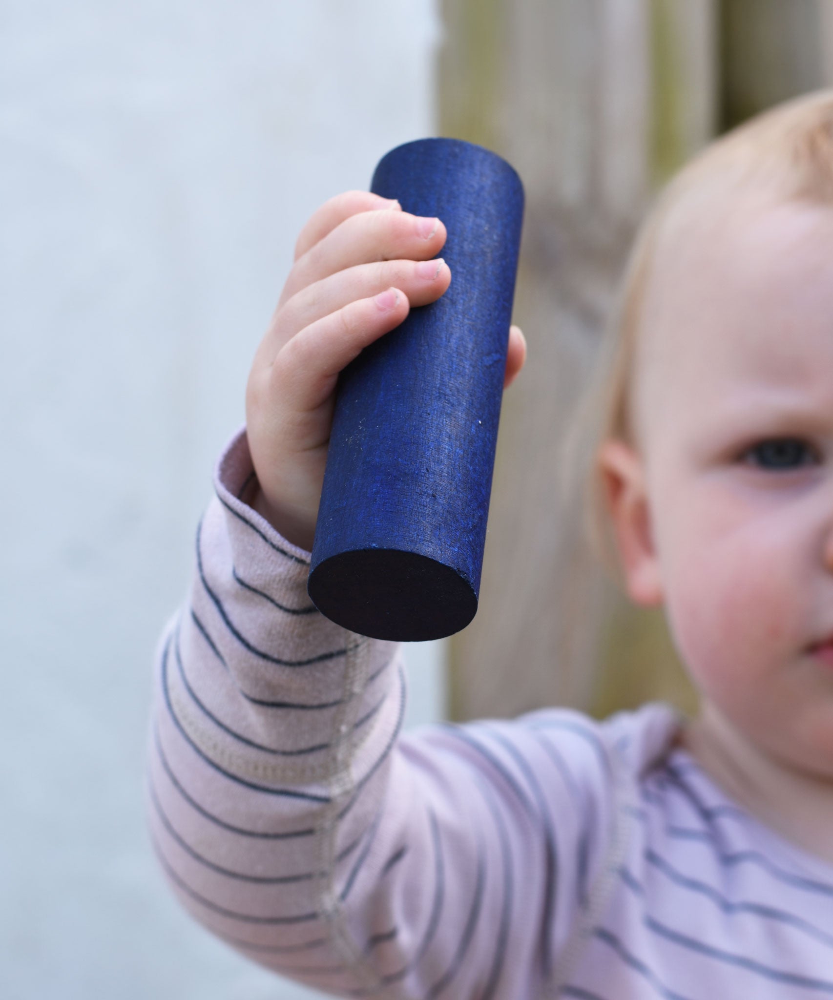 A close up of the large blue cylinder block in a young child's hand. 