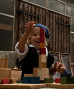 A child playing with Wooden Story Rainbow Blocks. The child is stacking the blocks on top of each other in a tower. 