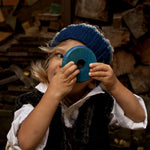 A child holding up a blue piece from the Wooden Story Rainbow Stacker up to their eye. They are peering through the hole in it's centre. 