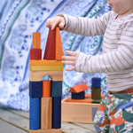 A young child playing with the Wooden Story Rainbow XL Blocks. The wooden tray can be seen in the background.