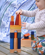A young child playing with the Wooden Story Rainbow XL Blocks. The wooden tray can be seen in the background.