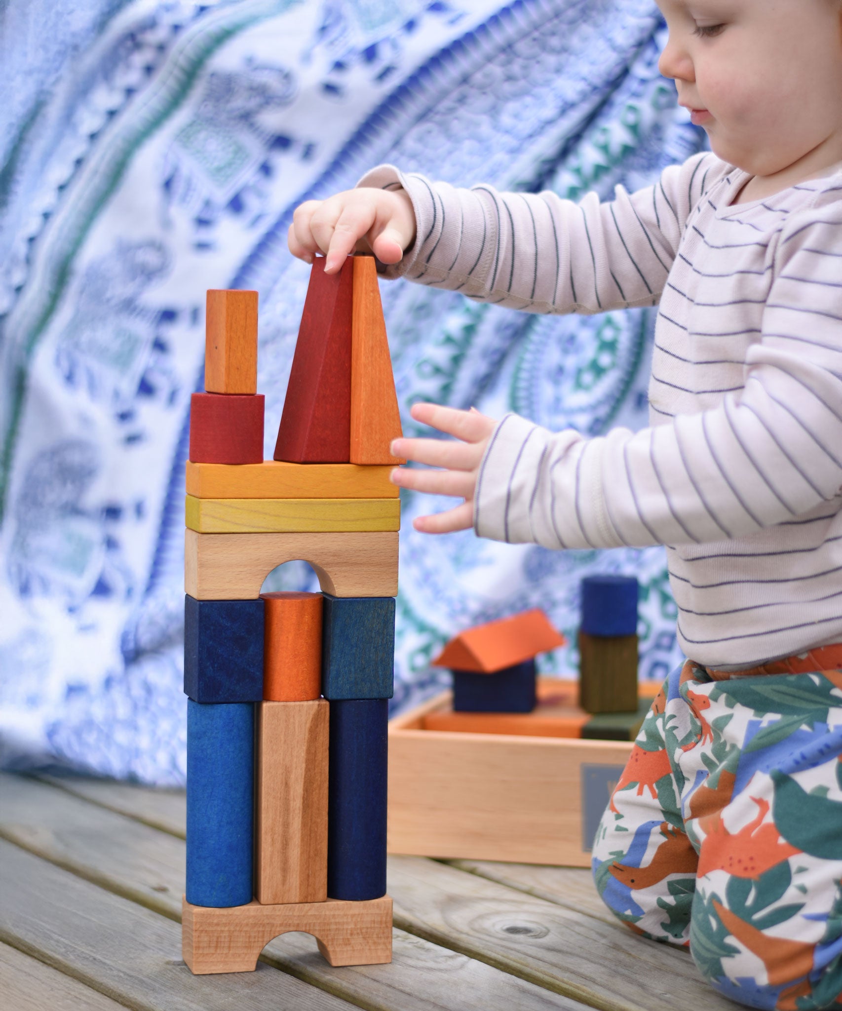 A young child playing with the Wooden Story Rainbow XL Blocks. The wooden tray can be seen in the background.