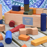 The blocks from the Wooden Story Rainbow XL Blocks set laid out on a wooden surface, the wooden storage box can be seen in the background.