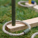 A close up of the Wooden Story logo that's engraved onto one of the base pieces of the  Ring Toss Game. The green stick piece can be seen with a green rope ring on it.