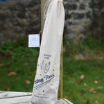 The Wooden Story Ring Toss Game shown in the cotton drawstring storage bag. The bag features beautiful traditional style typography and an illustration of the ring toss game. 
