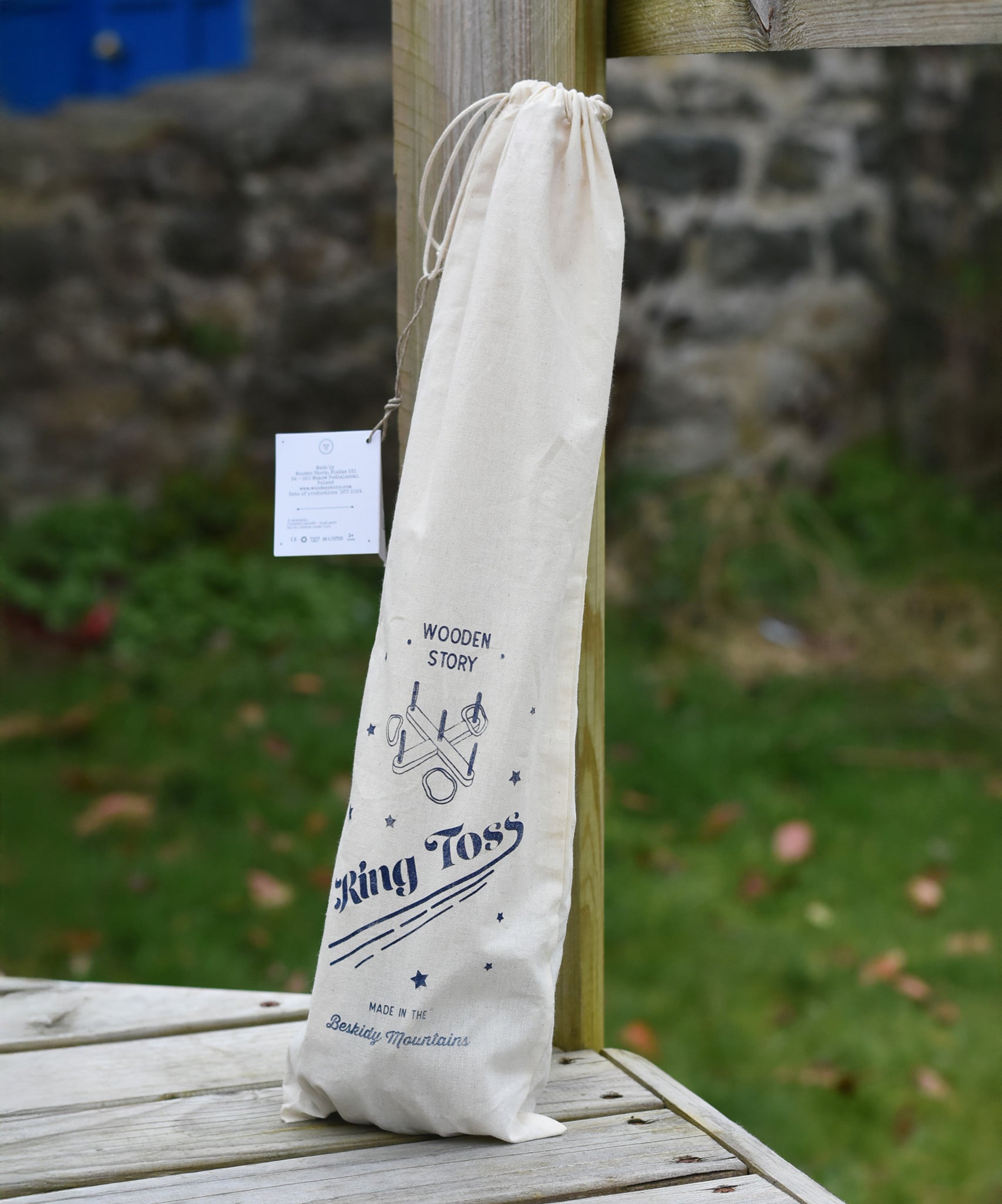 The Wooden Story Ring Toss Game shown in the cotton drawstring storage bag. The bag features beautiful traditional style typography and an illustration of the ring toss game. 