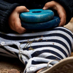 A close up of a child's hands holding to two blue pieces from the Wooden Story Rainbow Stacker.