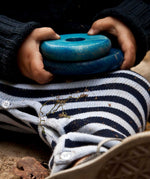 A close up of a child's hands holding to two blue pieces from the Wooden Story Rainbow Stacker.