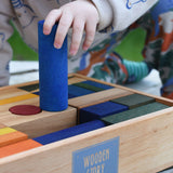 A close up of a child holding the large blue cylinder shaped block from the Wooden Story Rainbow XL Blocks set in their hand. 