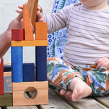A stack created with the blocks from the Wooden Story Rainbow XL Blocks An adult can be seen in the background passing a natural coloured block over to a young child.
