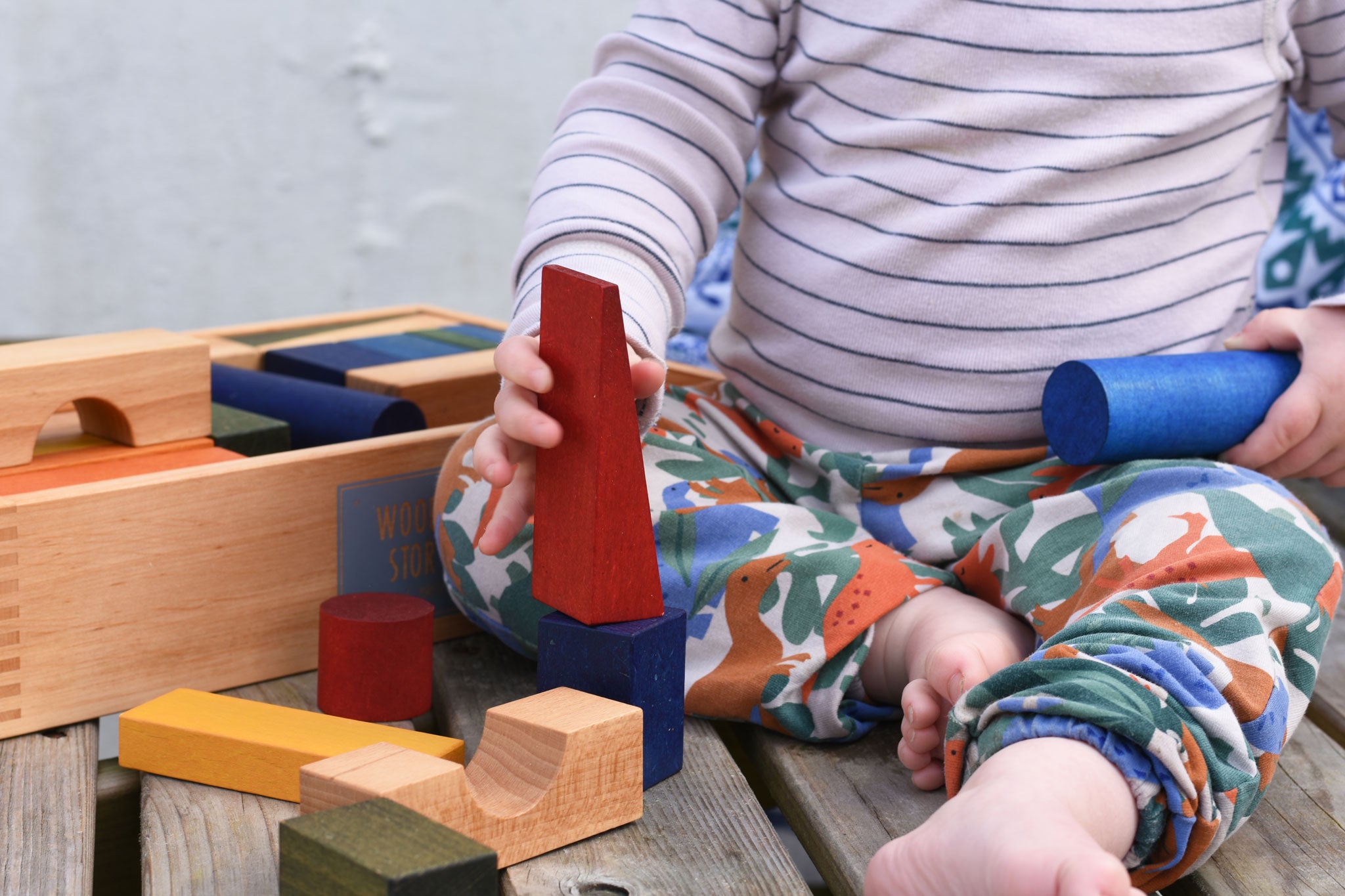 A child playing with the blocks from the Wooden Story Rainbow XL Blocks set. The wooden tray can be seen in the background.