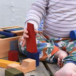 A child playing with the blocks from the Wooden Story Rainbow XL Blocks set. The wooden tray can be seen in the background.