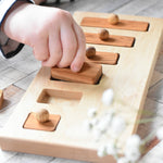 A close up of a child playing with the Wooden Story Long-Short Puzzle toy. The child is lifting a piece from the base of the puzzle.