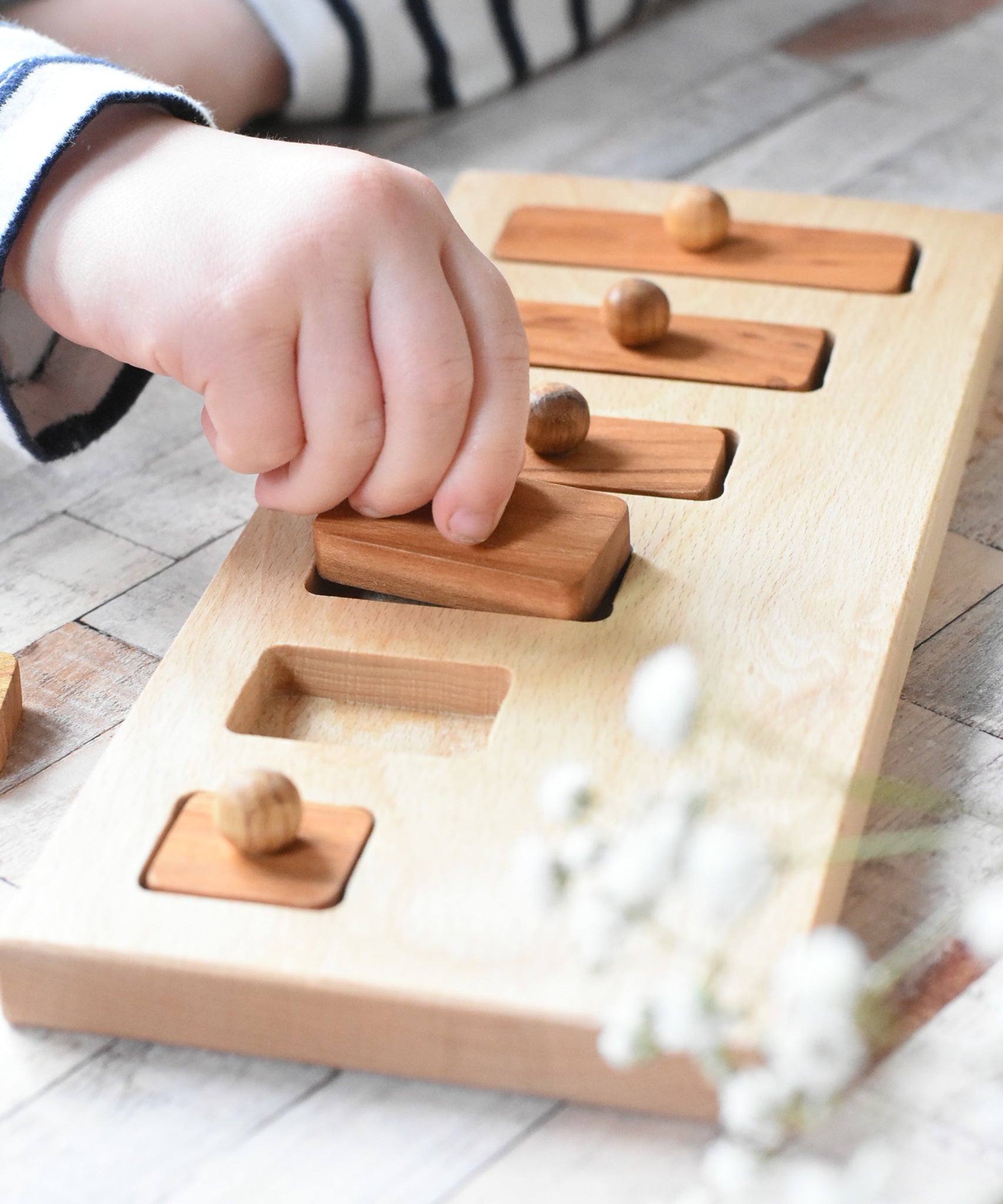 A close up of a child playing with the Wooden Story Long-Short Puzzle toy. The child is lifting a piece from the base of the puzzle.
