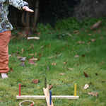 The Wooden Story Ring Toss Game in use on grass. A child can be seen standing on the side with one of the rings mid-air after being thrown.