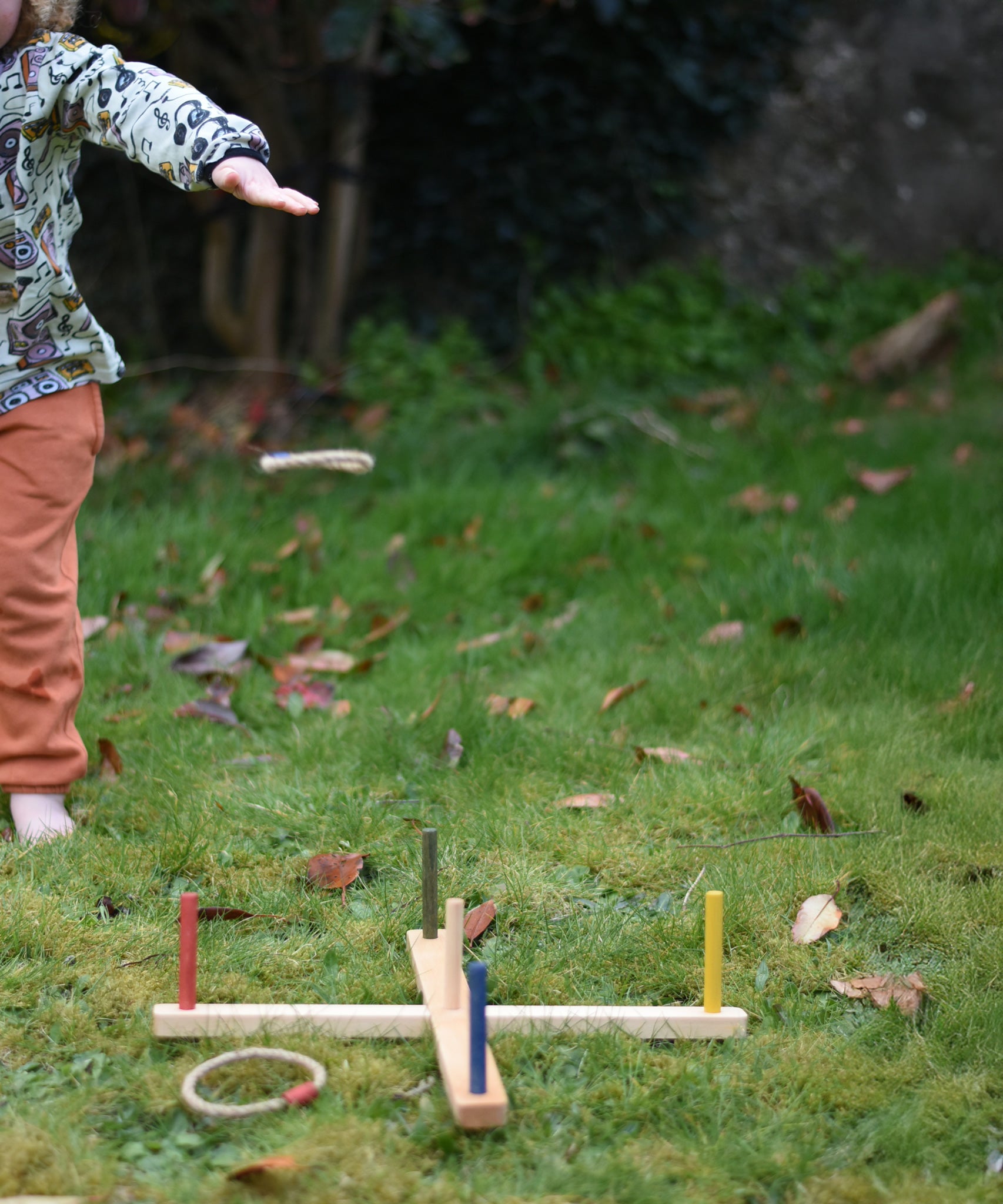 The Wooden Story Ring Toss Game in use on grass. A child can be seen standing on the side with one of the rings mid-air after being thrown.