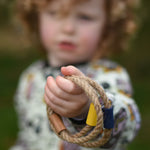 A close up of a child's hand holding  the rope rings from the Wooden Story Ring Toss Game. The Ring toss game is also know as Quoits or Hoopla. 