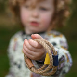 A close up of a child's hand holding  the rope rings from the Wooden Story Ring Toss Game. The Ring toss game is also know as Quoits or Hoopla. 