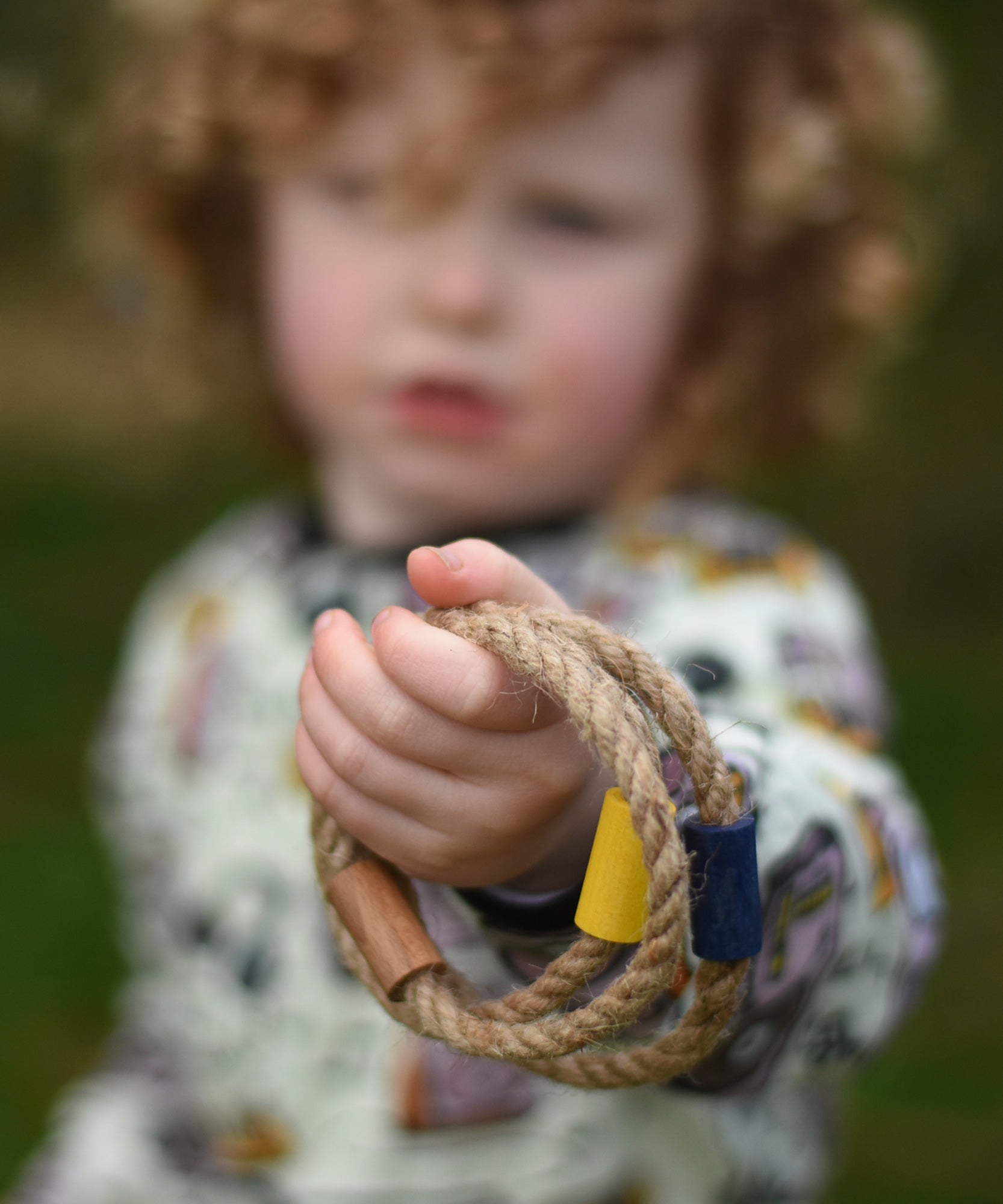 A close up of a child's hand holding  the rope rings from the Wooden Story Ring Toss Game. The Ring toss game is also know as Quoits or Hoopla. 