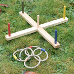 The Wooden Story Ring Toss Game set up on grass outdoors, the rings are placed next to the base and posts.