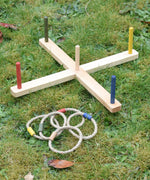 The Wooden Story Ring Toss Game set up on grass outdoors, the rings are placed next to the base and posts.