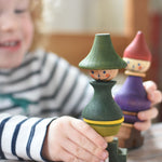 A close up of a child playing with the Wooden Story green stick figure stacking toy, the purple figure can be seen in the background.