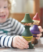 A close up of a child playing with the Wooden Story green stick figure stacking toy, the purple figure can be seen in the background.