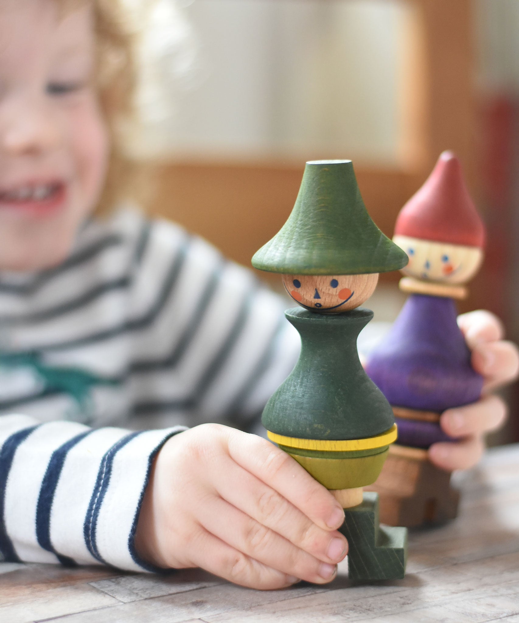 A close up of a child playing with the Wooden Story green stick figure stacking toy, the purple figure can be seen in the background.