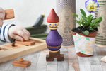 The Wooden Story Stacking Toy Stick Purple Number 6 Figure on a wooden surface. A child's hands can be seen in the background playing with the Wooden Story Long Short puzzle.
