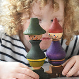 A close up of a child holding the Wooden Story green and purple stick figure stacking toys in their hands. 