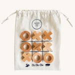 Wooden Story Tic Tac Toe game on a plain background. The wooden X and O pieces are placed on the drawstring bag which has the grid printed on it. 