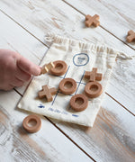 A close up of a child's hand playing with the Wooden Story Tic Tac Toe game.