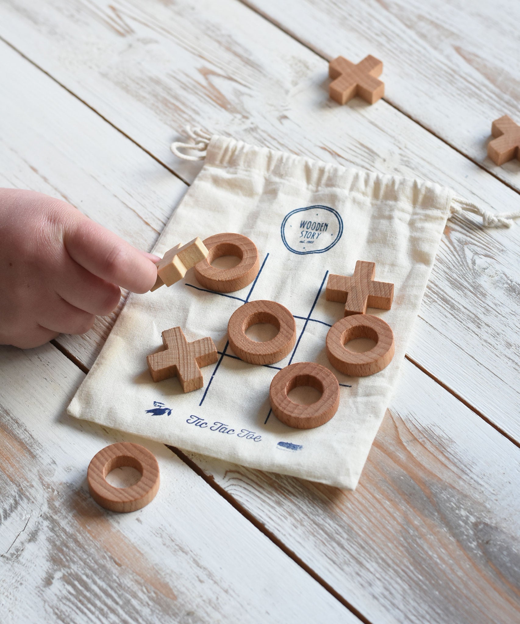 A close up of a child's hand playing with the Wooden Story Tic Tac Toe game.