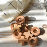 The wooden X and O pieces from the Wooden Story tic tac toe game laid out on a white wooden surface, the cotton drawstring storage bag can be seen in the background.