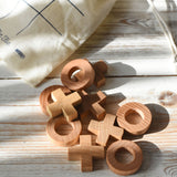 The wooden X and O pieces from the Wooden Story tic tac toe game laid out on a white wooden surface, the cotton drawstring storage bag can be seen in the background.