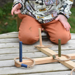 A close up of the Wooden Story Ring Toss Game set up on a wooden surface. A child can be seen in the background.