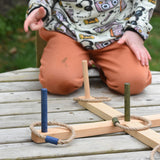 A close up of the Wooden Story Ring Toss Game set up on a wooden surface. A child can be seen in the background.