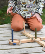 A close up of the Wooden Story Ring Toss Game set up on a wooden surface. A child can be seen in the background.