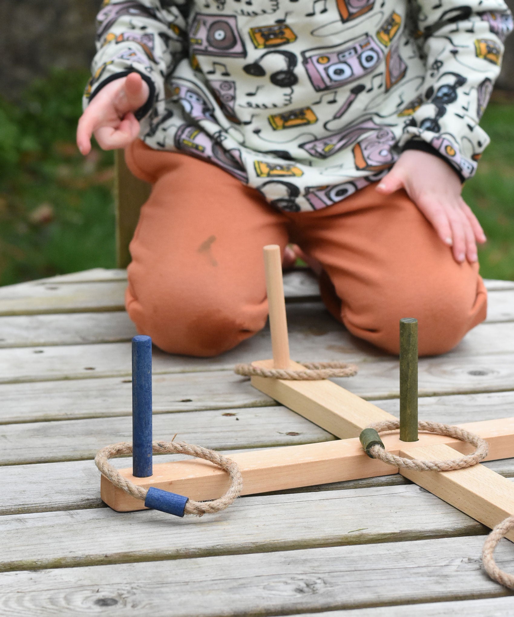 A close up of the Wooden Story Ring Toss Game set up on a wooden surface. A child can be seen in the background.